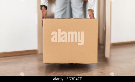 Paketzustellung. Nicht Erkennbare African American Lady Putting Big Cardboard Box Auf Dem Boden Betreten Nach Hause Nach Erhalt Paket Von Courier. 3/4-S Stockfoto