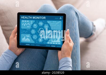 Nicht erkennbare Dame, die die mobile Anwendung des Gesundheitsmonitors auf einem digitalen Tablet verwendet, während sie sich zu Hause auf der Couch ausruhte und ihren Gesundheitszustand während ihres Aufenthalts überprüfte Stockfoto