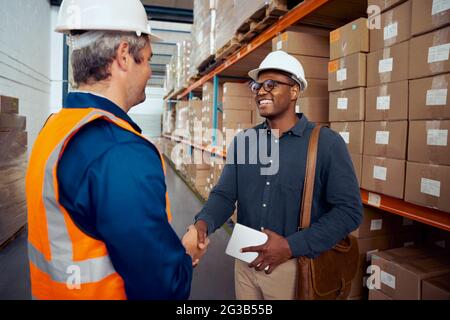 Afrikanischer Arbeiter schüttelt die Hand mit seinem Partner, der Schutzhelm trägt und das Tablet in der Hand hält Stockfoto