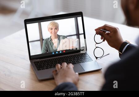 Konzept Der Online-Konferenz. Schwarzer männlicher Unternehmer mit Videoanruf mit junger Geschäftsfrau, macht Web-Meeting mit Laptop im Büro, genießen remo Stockfoto