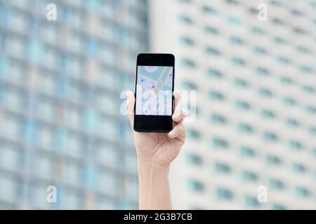 Nahaufnahme der männlichen Hand mit Smartphone und Online-Karte auf dem Bildschirm gegen das Stadtgebäude Stockfoto