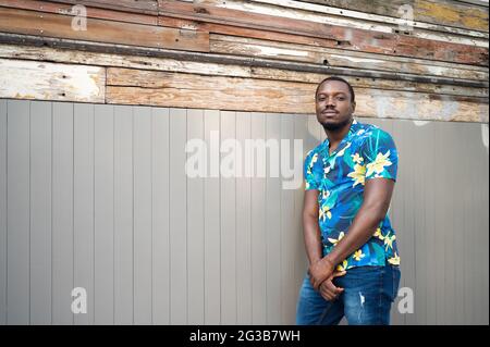 Junger Mann aus dem Exil trägt ein stilvolles blaues Hemd, das im Freien an der Wand lehnt Stockfoto