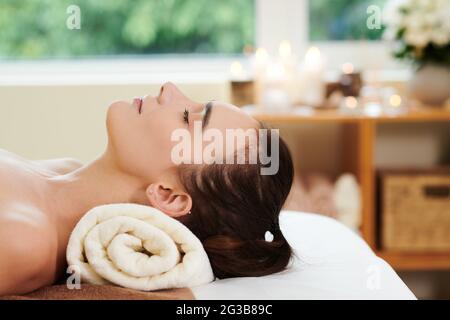 Junge schöne Frau, die mit geschlossenen Augen liegt und sich im Spa entspannt Stockfoto