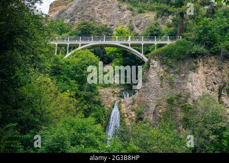 Wunderschöne Sommerlandschaft des Botanischen Gartens – Tiflis, Georgien – üppiges Laub, Berge, Brücke und Wasserfall. Stockfoto