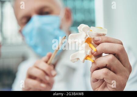 Arzt in einer Gesichtsmaske, die die Anatomie der Wirbelsäule erklärt Stockfoto