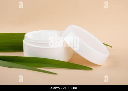 Kosmetische Creme und grünes Blatt auf beigem Hintergrund. Hautpflege. Stockfoto