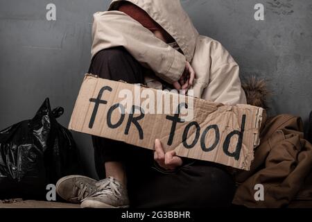 Ein Bettler bittet um Essen mit einem Zeichen für Hilfe. Stockfoto