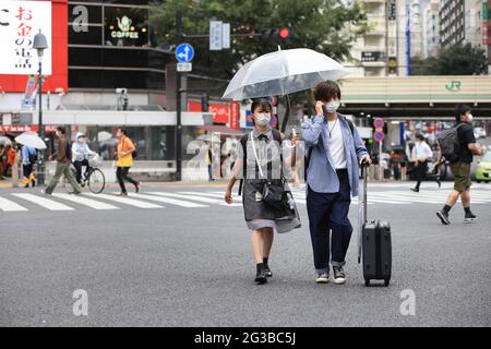 Touristen, die Gesichtsmasken als Schutzmaßnahme gegen Covid-19 tragen, halten einen Regenschirm in der Nähe des Shibuya Crossing.die japanische Meteorologische Agentur gab bekannt, dass die diesjährige Regenzeit in Tokio und Kanto-Koshin im Osten und im Zentrum Japans sieben Tage später als durchschnittlich und drei Tage später als zuletzt begann Jahr am 14. Juni 2021. Stockfoto