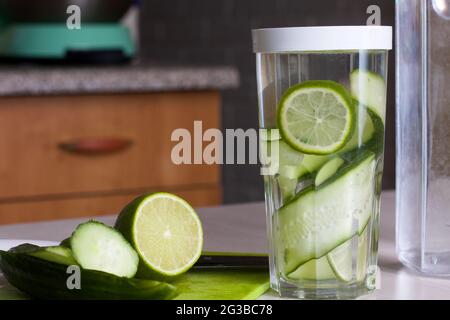 Gurken- und Limettenscheiben werden in einem Glas mit Wasser gefüllt. Kochendes Wasser mit Kalk und Gurke. Rezept für Entgiftung von Wasser. Stockfoto