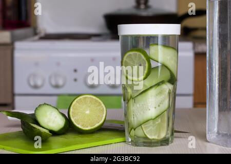 Gurken- und Limettenscheiben werden in einem Glas mit Wasser gefüllt. Kochendes Wasser mit Kalk und Gurke. Rezept für Entgiftung von Wasser. Stockfoto