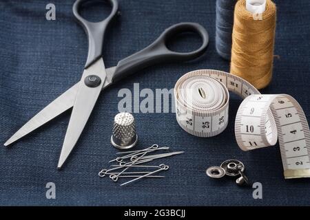 Scheren, Nimble, Stifte, Zentimeter-Klebeband, Gewinde, Knopf Auf Schwarzem Jeans Stoff Close Up Und Draufsicht. Stockfoto