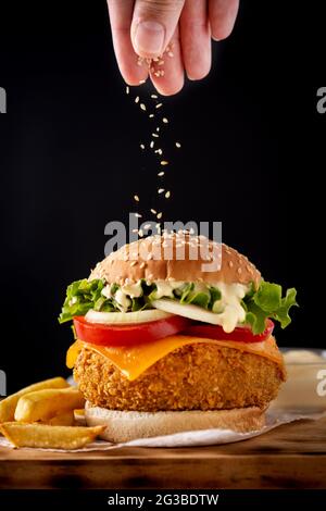 Sesamsamen auf knusprigen Chicken Burger auf schwarzem Hintergrund gießen Stockfoto