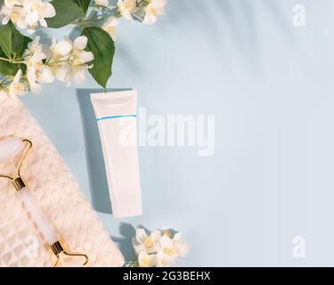 Sommer Spa Relax Komposition mit Kosmetikschlauch, Handtuch, Gesichtswalze und jasmin Blumen auf blauem Hintergrund mit Kopierfläche. Kosmetisches Modell Stockfoto