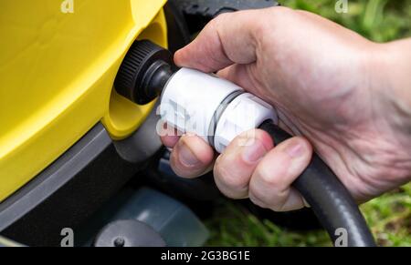 Mit der männlichen Hand wird die Schnellverschluss-Schlauchkupplung für Wasser aus nächster Nähe auf den Druckreiniger gesetzt. Industrie Stockfoto