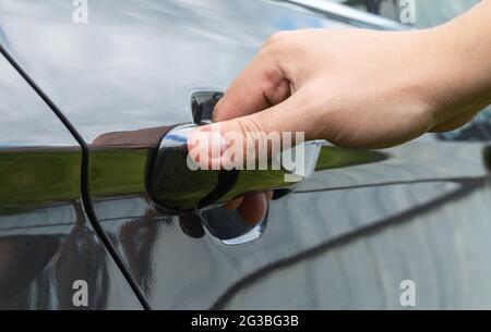 Die Hand eines Mannes öffnet eine Autotür. Konzept für Autodiebstahl, Makro Stockfoto