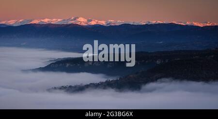 Sonnenaufgang von der Roca del Migdia Klippe mit Blick auf die Plana de Vic mit Nebel und den östlichen Pyrenäen im Hintergrund (Osona, Katalonien, Spanien) Stockfoto