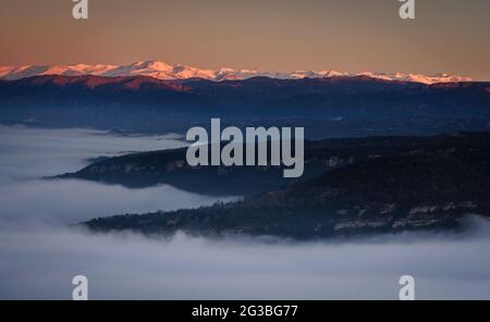 Sonnenaufgang von der Roca del Migdia Klippe mit Blick auf die Plana de Vic mit Nebel und den östlichen Pyrenäen im Hintergrund (Osona, Katalonien, Spanien) Stockfoto