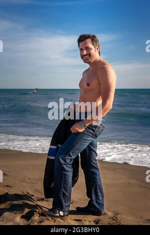 Mann, der am Strand am Meer steht und am schönen sonnigen Frühlingstag glücklich lächelt. Stockfoto