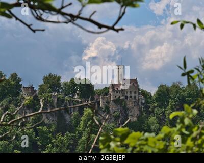 Schöne Aussicht auf das berühmte historische Wahrzeichen Schloss Lichtenstein auf einem Felsen am Rande der Schwäbischen Alb, Deutschland durch Äste von Bäumen gesehen. Stockfoto