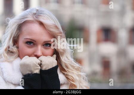 Nachdenkliche, junge blonde Frau, die ihre Handgeläute in einem Nahaufnahme-Porträt im Freien an einem kalten Wintertag mit Copyspace an ihr Gesicht hält Stockfoto