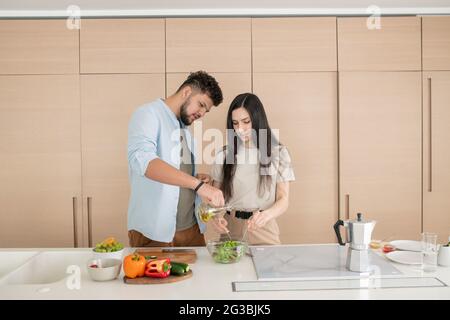Junger Mann gießt Olivenöl in eine Schüssel mit Gemüsesalat Stockfoto