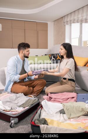 Glückliches Paar, das während der Reise Kleidung in Koffer packt Stockfoto