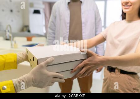 Die Hände des Kurierers, der die Schachtel mit Pizza an die junge Frau übergab, waren mit Handschuhen überreicht Stockfoto