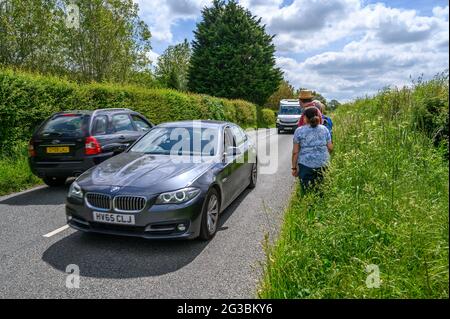 Eine Gruppe von Wanderern steht am Grasrand, während der Verkehr entlang der South Road zwischen Plumpton Green und South Chailey, East Sussex, Engl, vorbeifährt Stockfoto