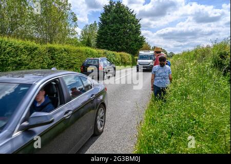 Eine Gruppe von Wanderern steht am Grasrand, während der Verkehr entlang der South Road zwischen Plumpton Green und South Chailey, East Sussex, Engl, vorbeifährt Stockfoto