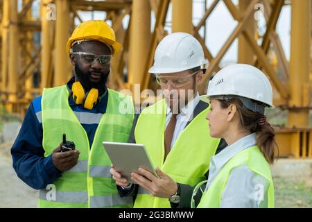 Eine Gruppe junger interkultureller Bauherren, die sich das Tablet-Display ansieht Stockfoto