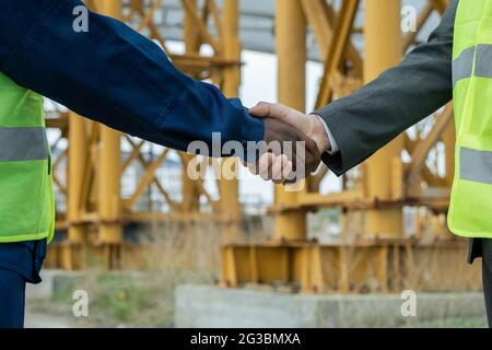 Handschlag von Ingenieuren afrikanischer und kaukasischer Ethnien gegen Baustelle Stockfoto