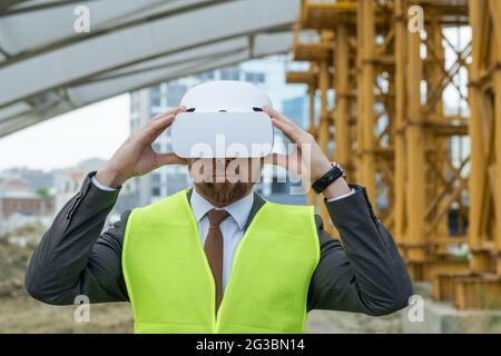 Zeitgemäßer Bauunternehmer in Anzug und vr Headset, der sich auf der Baustelle umsieht Stockfoto