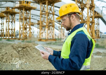 Seriöse Ingenieur in Arbeitskleidung Blick auf Skizze des Gebäudes auf Tablet-Bildschirm Stockfoto