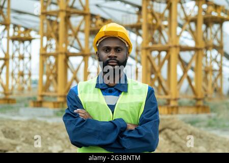 Junger afrikanischer Bauarbeiter in Uniform und Hardhat, der Arme an Brust kreuzt Stockfoto