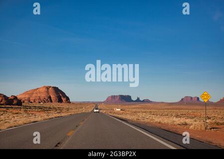 Blick auf einem langen Straßenabschnitt durch die Halbwüste in Arizona auf dem Weg zum Monument Valley mit felsigen Aufschlüssen oder Buttes in der Ferne, den USA Stockfoto