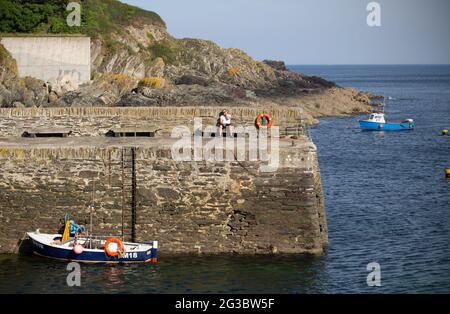 Ein Mann nimmt einen ‘Verschnaufpause’ an der Hafenmauer in dem kleinen Fischerdorf und Hafenstadt Polperro im Süden von Cornwall. Wie die Coronavirus-Pandemie Stockfoto