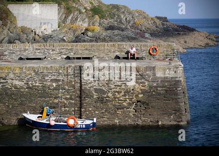 Ein Mann nimmt einen ‘Verschnaufpause’ an der Hafenmauer in dem kleinen Fischerdorf und Hafenstadt Polperro im Süden von Cornwall. Wie die Coronavirus-Pandemie Stockfoto