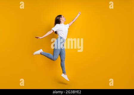 In voller Länge Körpergröße Foto von sorglosen Mädchen mit langen Haaren springen halten Hand nach oben Stellen Sie sich isoliert auf hellen gelben Hintergrund Stockfoto