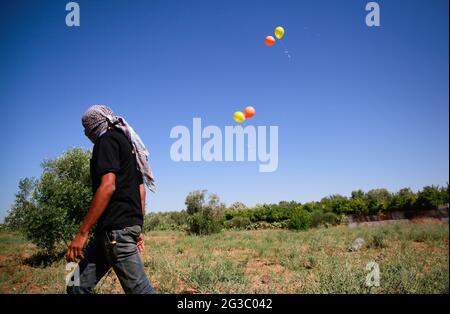 Gaza, Palästina. Juni 2021. Maskierter Palästinenser geht weg, nachdem er brennende Ballons in Richtung Israel abgeschossen hat. Palästinensische Aktivisten starten brennende Ballons aus dem Gazastreifen in Richtung Israel, um gegen den derzeit stattfindenden flaggenmarsch in Ostjerusalem zu protestieren und um einen erneuten Ausbruch von Gewalt zu sorgen, da etwa 5,000 rechte Nationalisten mit der blau-weißen Flagge Israels durch die Jerusalemer Altstadt ziehen werden. Gaza-Brandballons verbrannten Ackerland an mindestens 13 verschiedenen Orten, berichtet israelische Medien. Kredit: SOPA Images Limited/Alamy Live Nachrichten Stockfoto