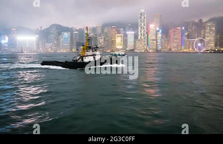 Schlepper im Hafen von Hongkong am frühen Abend mit Stadtkulisse. Stockfoto