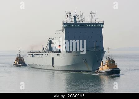 Die mächtigen Schlepper führen das Royal Fleet Auxiliary Schiff CARDIGAN BAY in Richtung Hafenmündung Stockfoto