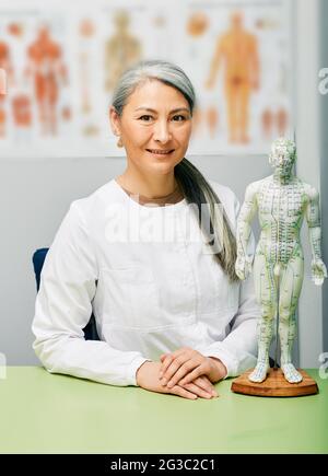 Reife Akupunkturistin, Ärztin für traditionelle chinesische Medizin an ihrem medizinischen Arbeitsplatz Stockfoto