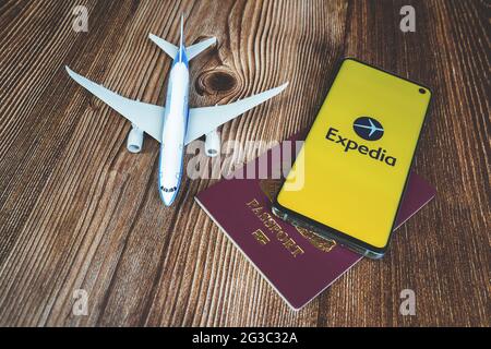 Smartphone mit Expedia App-Logo mit Flugzeugspielzeug und rotem Reisepass auf Holzhintergrund. Reise-Anwendung, Urlaubsplanung Stockfoto