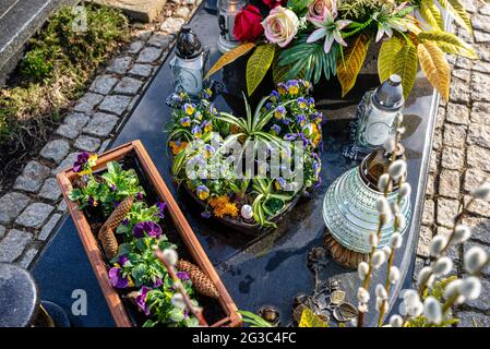 Violette Stiefmütterchen und Fichtenkegel in einem herzförmigen Topf, der auf einem Grabstein auf einem christlichen Friedhof steht. Stockfoto