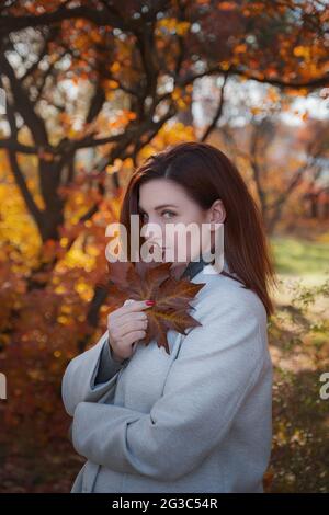 Eine niedliche rothaarige Frau in guter Laune posiert an einem Herbsttag und genießt das schöne Wetter. Das Konzept und die Idee, Herbst und Herbst Getaway zu genießen Stockfoto