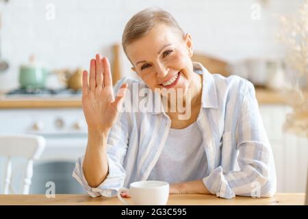 Glückliche Rentnerin winkte der Kamera beim Videoanruf zu Hause zu und grüßte sie Stockfoto