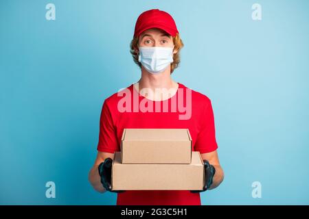 Porträt von schönen Briefträger Hände halten Kartons tragen medizinische kalte Gesundheitsmaske isoliert auf blauem Hintergrund Stockfoto