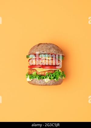 Seitenansicht von oben mit einem veganen Burger auf einem orangen Tisch. Hausgemachter Burger mit Sojapasteten als Fleischersatz, veganem Käse und Remoulade und f Stockfoto