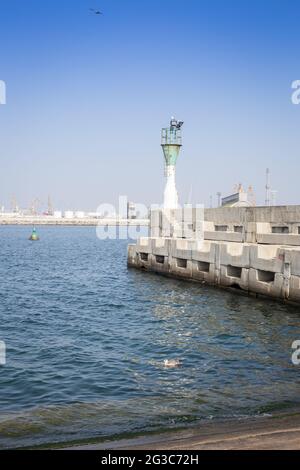 Kleiner Leuchtturm im Hafen vor dem Hintergrund eines blauen Himmels mit weißen Wolken Stockfoto