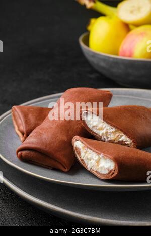 Nahaufnahme von dünnen Schokoladenpfannkuchen, gefüllt mit Quark, Banane und Apfel Stockfoto